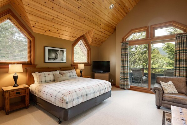 A bedroom with a bed, a TV, a sofa, and large windows.
