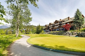 A lodge with a curved driveway, surrounded by lush greenery and mountains in the background.