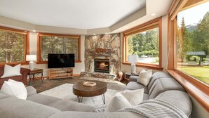 Un salón con chimenea de piedra, ventanas amplias y un televisor de pantalla plana.