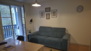 A living room with a grey sofa, a wooden table, and a clock on the wall. - 3-Bedroom Apartment with Parking and Ski Locker, Cauterets (Cauterets)