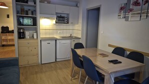A compact kitchen with a microwave, oven, and dishwasher. There is a dining table with chairs and a small bookshelf. - 3-Bedroom Apartment with Parking and Ski Locker, Cauterets (Cauterets)