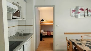 A compact kitchen with a microwave, sink, and wooden table. A bunk bed is visible in the adjacent room. - 3-Bedroom Apartment with Parking and Ski Locker, Cauterets (Cauterets)