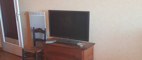 Una sala de estar con una televisión sobre un mueble de madera, una silla de mimbre y un sofá.