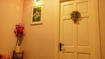 Eine weiße Tür mit einem floralen Kranz, ein kleiner Topfpflanze mit roten Blüten und ein gerahmtes Bild an der Wand.
