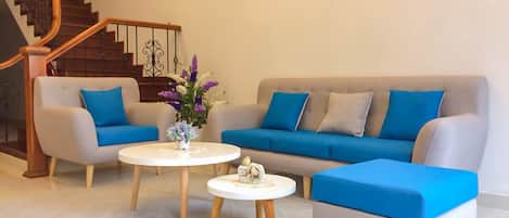 Relax in this stylish living room with a sofa, ottoman, and coffee tables, plus a staircase and framed artwork.