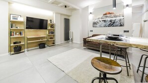 Una sala de estar moderna con un televisor de pantalla plana, estanterías de madera, una mesa de comedor con taburetes altos y un cuadro abstracto grande en la pared.
