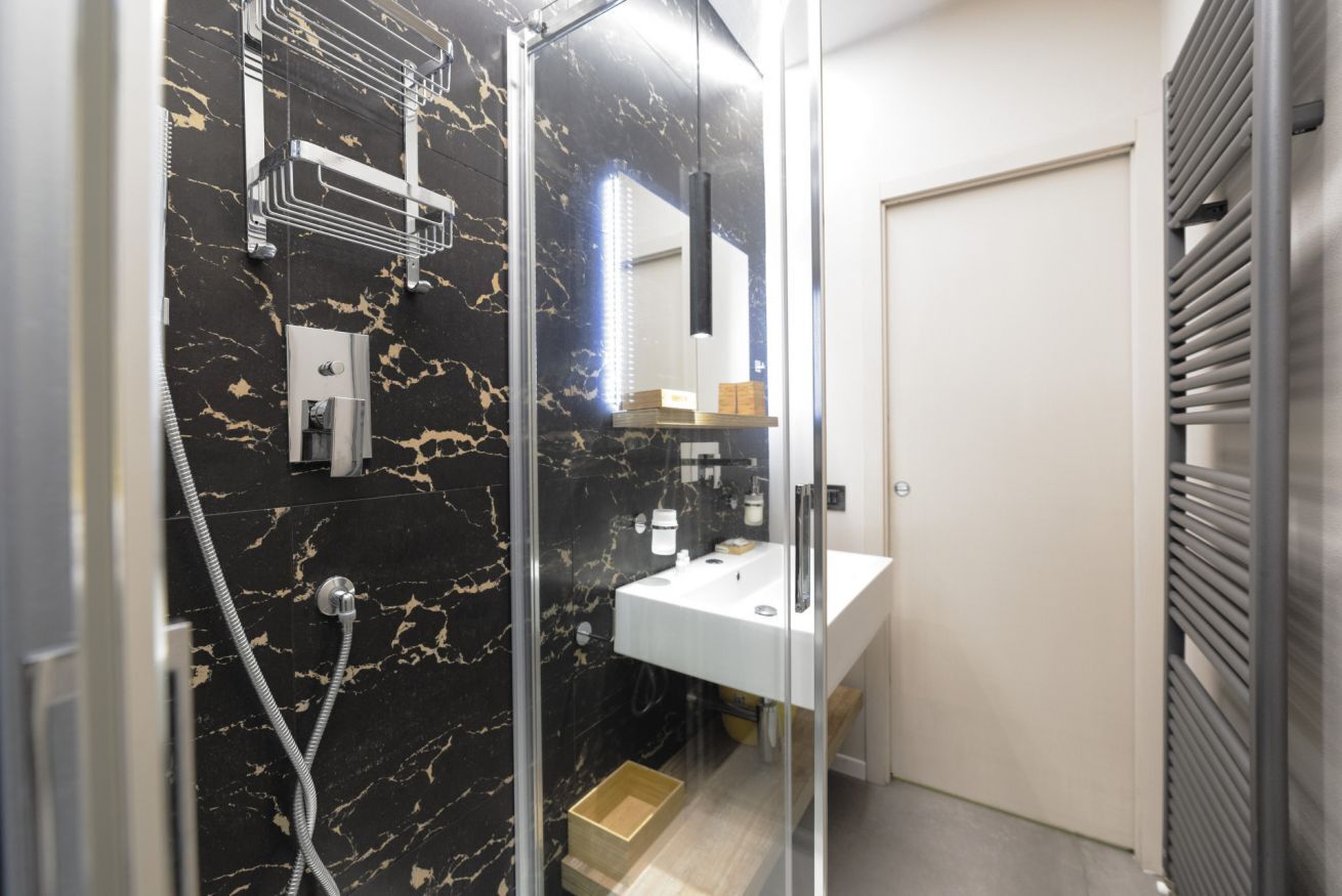 A modern bathroom with a glass shower enclosure, a white sink, and a marble-tiled wall.