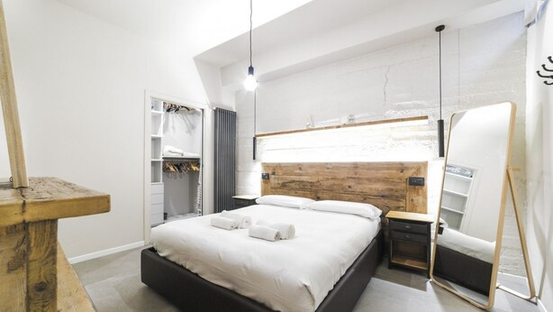 Un dormitorio moderno con cabecera de madera, una mesita de noche, un armario y un espejo grande.