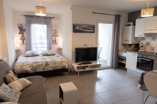 A modern bedroom with a bed, TV, and kitchenette.