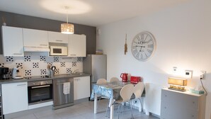 Una cocina moderna con armarios blancos, microondas, horno de acero inoxidable y una mesa de comedor con sillas.