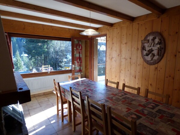 A dining area with a large table and chairs, wooden walls, a view of trees, and a decorative plate on the wall.