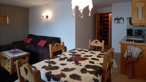 A cozy living room with a dark sofa, a small wooden table, and a dining table with a cow print tablecloth.