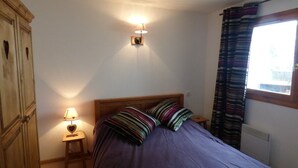 A bedroom with a bed, a nightstand, a lamp, a wardrobe, and a window with curtains.