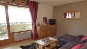 A living room with a sofa, a coffee table, a TV on a wooden cabinet, and a window with curtains.