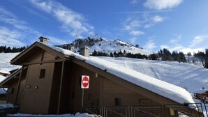 A wooden building with a snow-covered roof, a 'no entry' sign, and a mountainous backdrop.