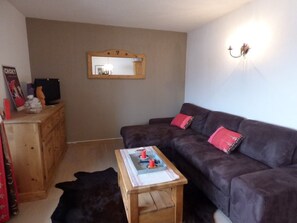 Uma sala de estar com um sofá cinza escuro, uma mesa de centro de madeira, um espelho na parede e um pequeno armário de madeira.
