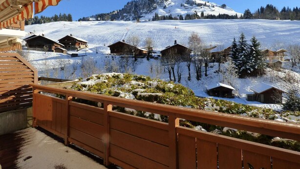 A chalet-style building with a wooden balcony overlooking a snow-covered mountain.