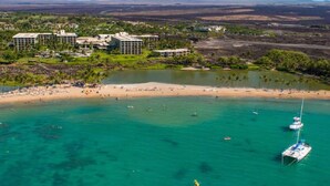 A coastal resort with multiple buildings, a sandy beach, and clear turquoise waters. - Corner Villa with Golf Course Views | Steps from Waikoloa Shops & Beaches (Waikoloa Village)