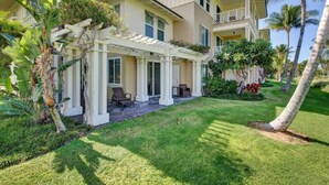 A two-story house with a covered patio, lush greenery, and palm trees. - Corner Villa with Golf Course Views | Steps from Waikoloa Shops & Beaches (Waikoloa Village)