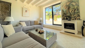 Una sala de estar con sofá, una mesa de centro de vidrio, chimenea y un ventanal con vistas a la vegetación.