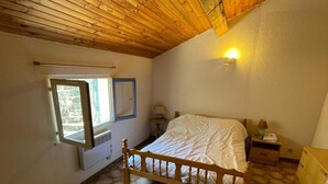 Ein Schlafzimmer mit Holzbalkendecke, einem Bett mit weißer Matratze, einem Fenster mit blauem Rahmen und sechseckischem Fliesendesign.