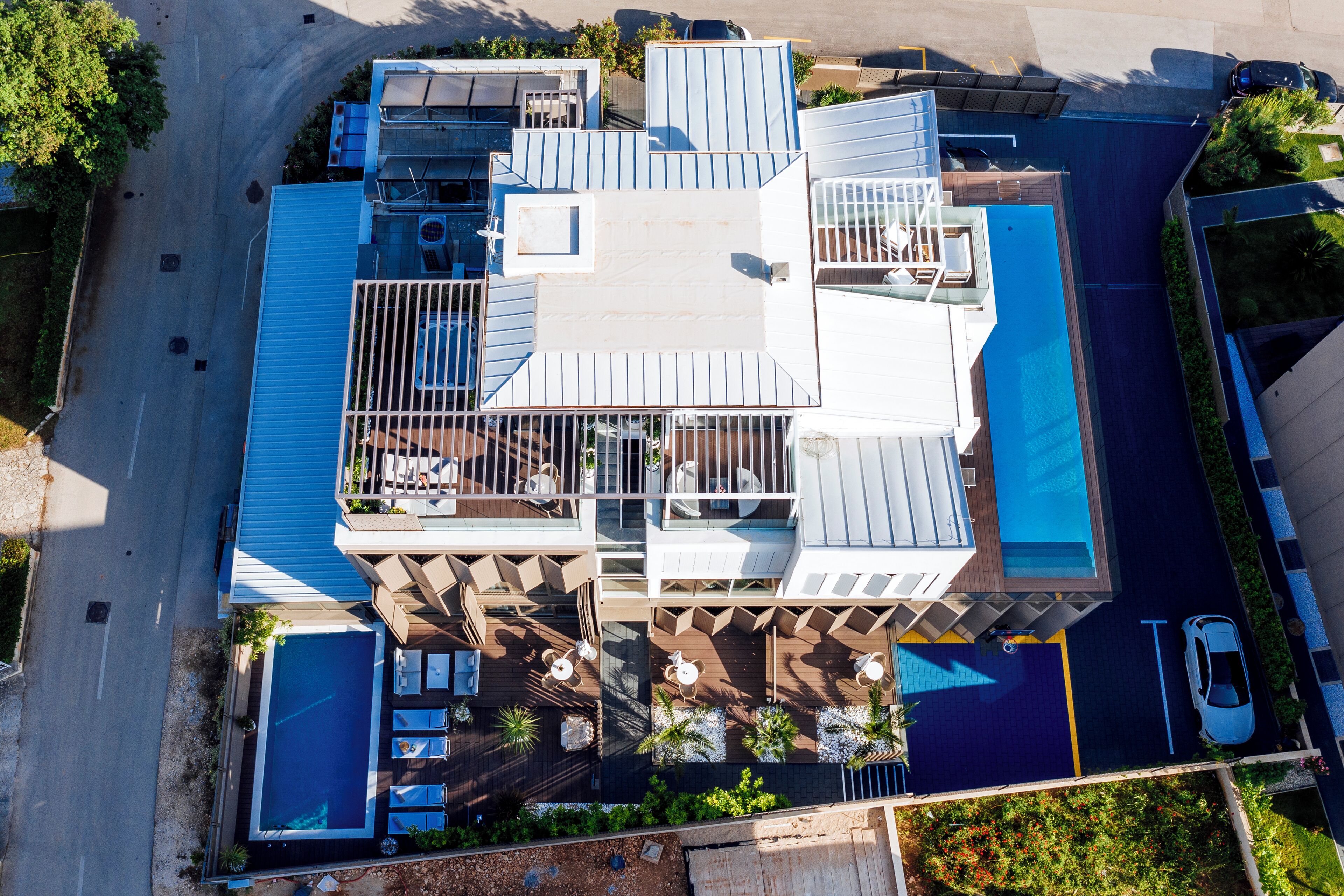 Vista aérea de um hotel moderno com piscina no terraço, várias varandas e área de estacionamento.
