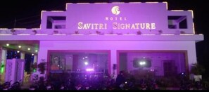 The exterior of the Savitri Signature Hotel with illuminated signage and a crowd of people in front. - Hotel Regal (Jabalpur)