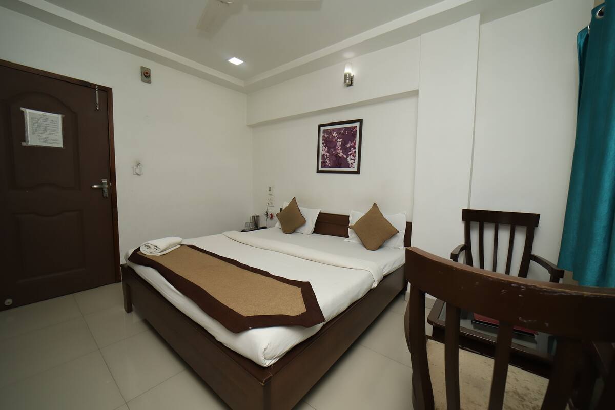 A neatly arranged hotel room with a bed, a chair, a desk, and a door.