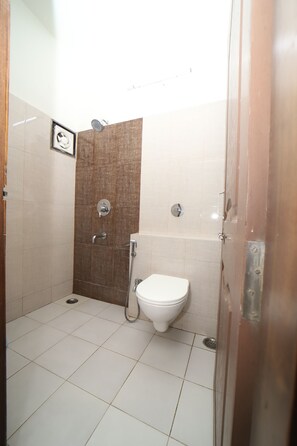 A bathroom with a shower, toilet, and a tiled floor. - Hotel Regal (Jabalpur)