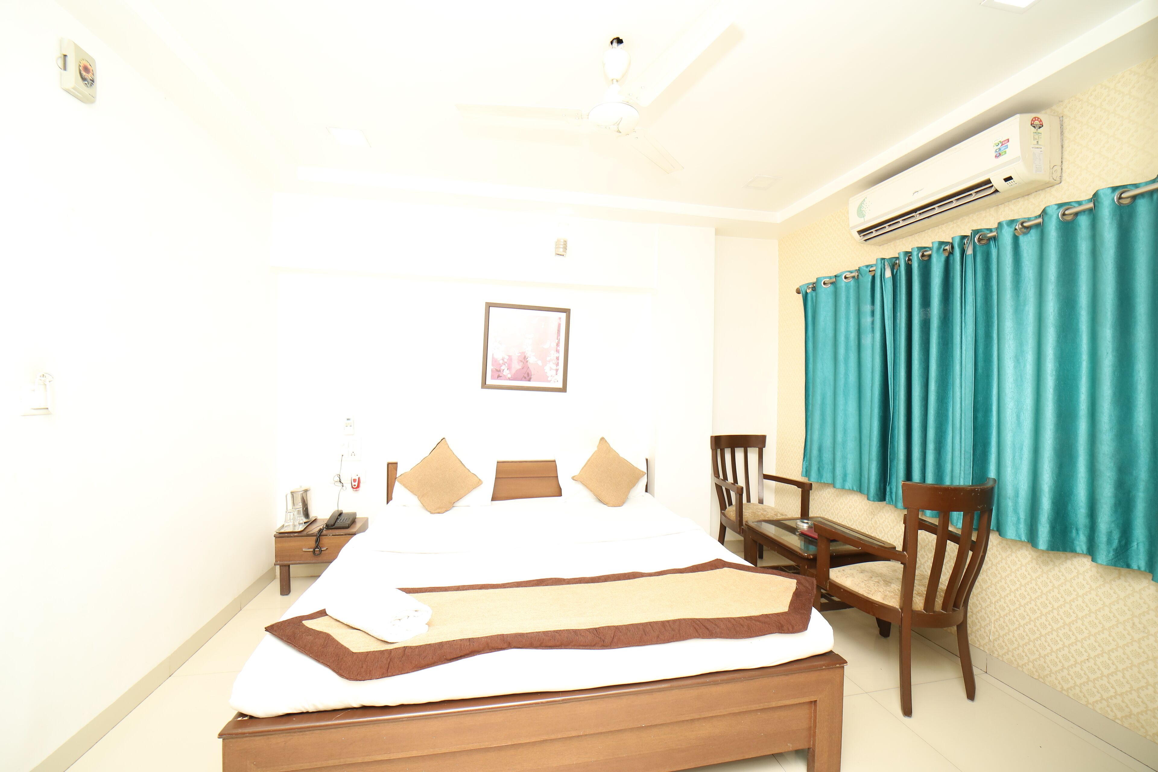 Habitación de hotel con cama, escritorio, silla, aire acondicionado y ventana con cortinas.