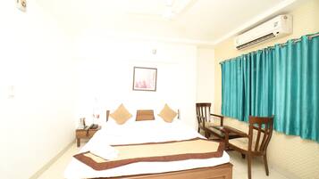 Habitación de hotel con cama, escritorio, silla, aire acondicionado y ventana con cortinas.