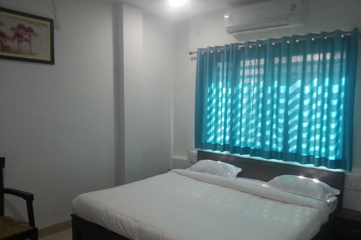A bedroom with a bed, a chair, a nightstand, and a window with curtains.