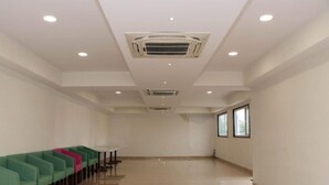 A spacious room with a long row of green and pink chairs, a white table, and a ceiling air conditioning unit. - Hotel Regal (Jabalpur)