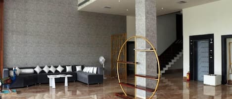 Um lobby moderno com um sofá preto, mesa de centro branca e uma peça decorativa única em dourado e madeira.