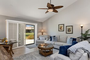 A spacious living room with a large sliding glass door leading to a patio, a ceiling fan, a round coffee table, and a sofa with cushions. - Two King 👑 Suite,🌴Cozy Palm Desert Condo Getaway ♥️ Great for Extended Stays! (Palm Desert)