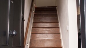 Un escalier en bois, avec une porte sombre en haut et un mur blanc orné d’un cadre photo en bas.