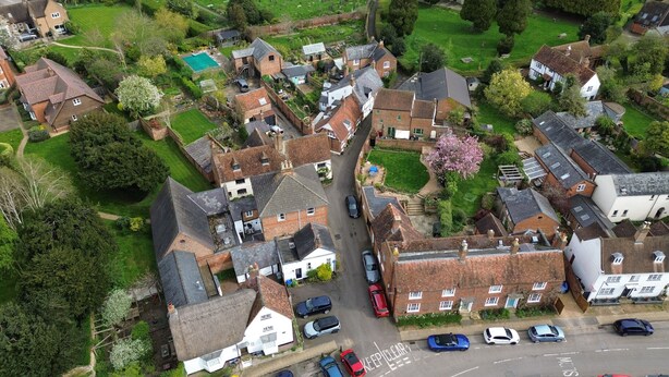 Vue aérienne d’un quartier résidentiel avec des maisons, une rue étroite et des voitures garées.