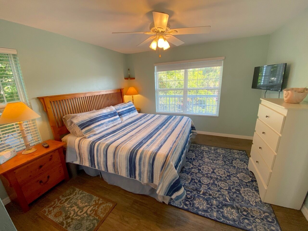 Une chambre à coucher comprenant un lit, une table de chevet, une commode et un ventilateur de plafond.