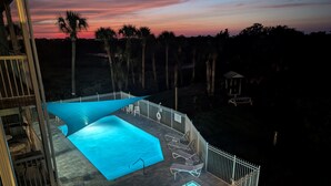 Zona de piscina en la azotea con vista al atardecer, rodeada de palmeras y una valla blanca.