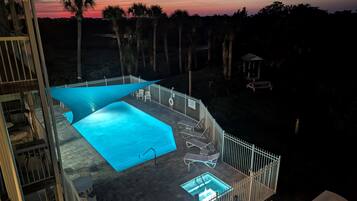 A rooftop pool area with a view of the sunset, surrounded by palm trees and a white fence.