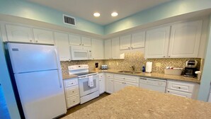 Una cocina con armarios blancos, encimera de granito, refrigerador, horno, microondas y pileta.