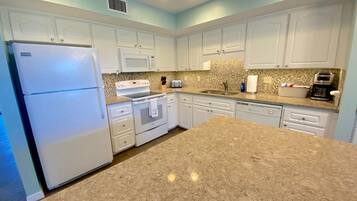 A kitchen with white cabinets, a granite countertop, a refrigerator, an oven, a microwave, and a sink.
