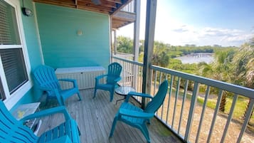 A covered deck with blue chairs and a table, overlooking a body of water and greenery.