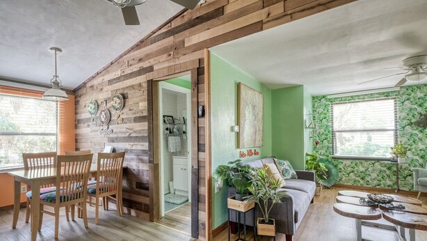 A modern living room with a wooden accent wall, a dining area with wooden chairs, a sofa, and a coffee table. - Hawthorne - Fisherman's Delight! Plenty of Parking (Cedar Key)