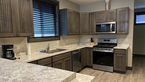A modern kitchen with granite countertops, stainless steel appliances, and wooden cabinetry. - Modern condominium in Ennis (Ennis)