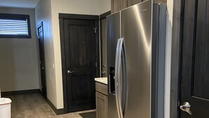 A modern kitchen with dark wooden cabinets, a stainless steel refrigerator, and a window with blinds. - Modern condominium in Ennis (Ennis)