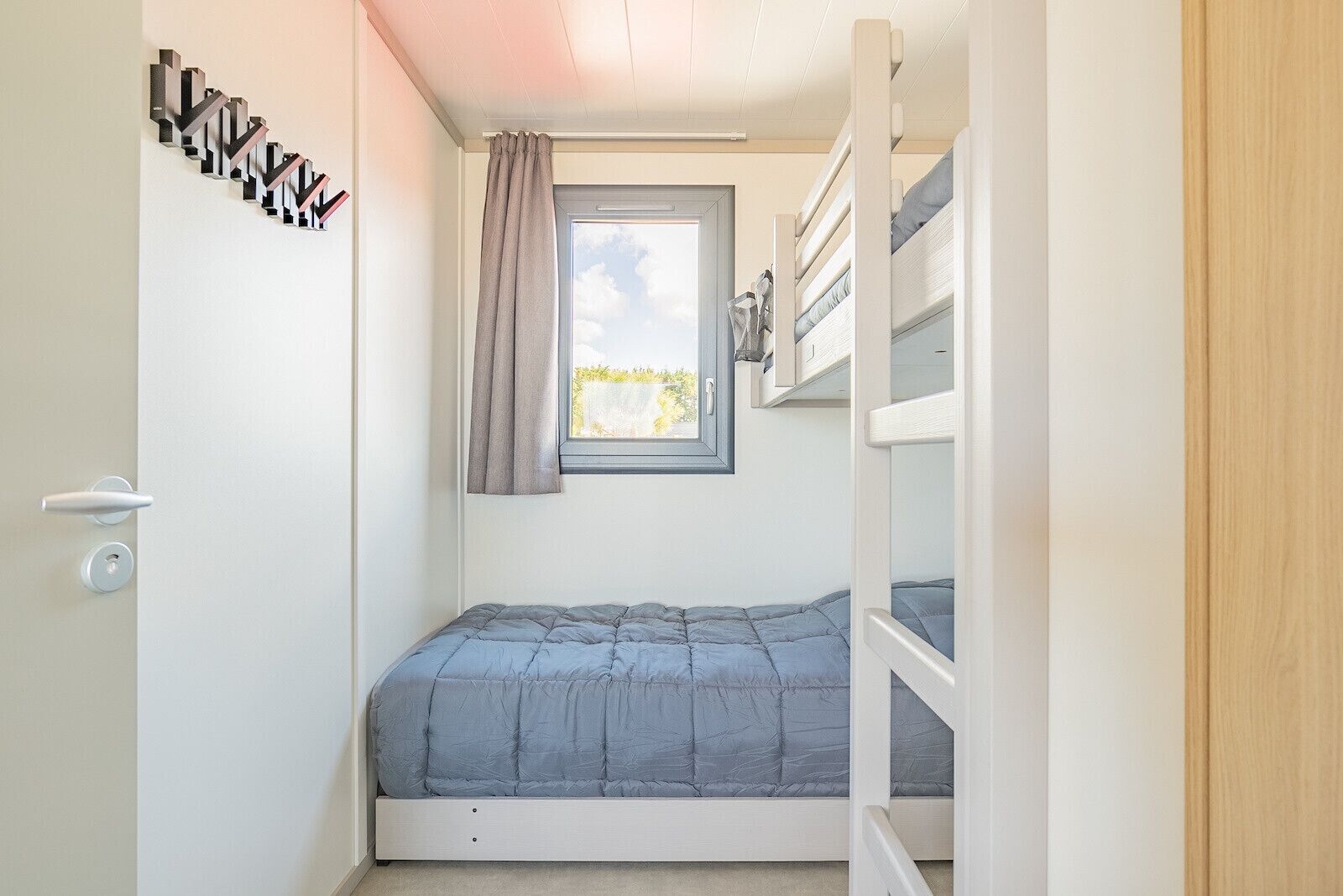 Una habitación pequeña con una cama litera, una ventana con cortinas y una puerta con picaporte moderno.
