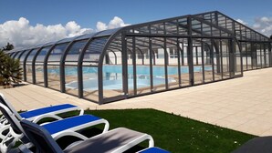 Un área de piscina con paredes de vidrio, sillas de descanso y cielo despejado.