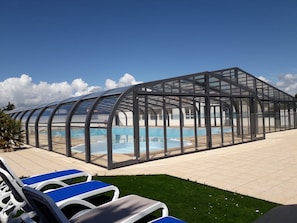 Ein Poolbereich mit Glasumrandung, Liegestühlen und blauem Himmel.