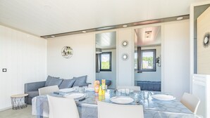 Un comedor moderno con una mesa redonda dispuesta para cuatro, sillas blancas y un sofá al fondo.